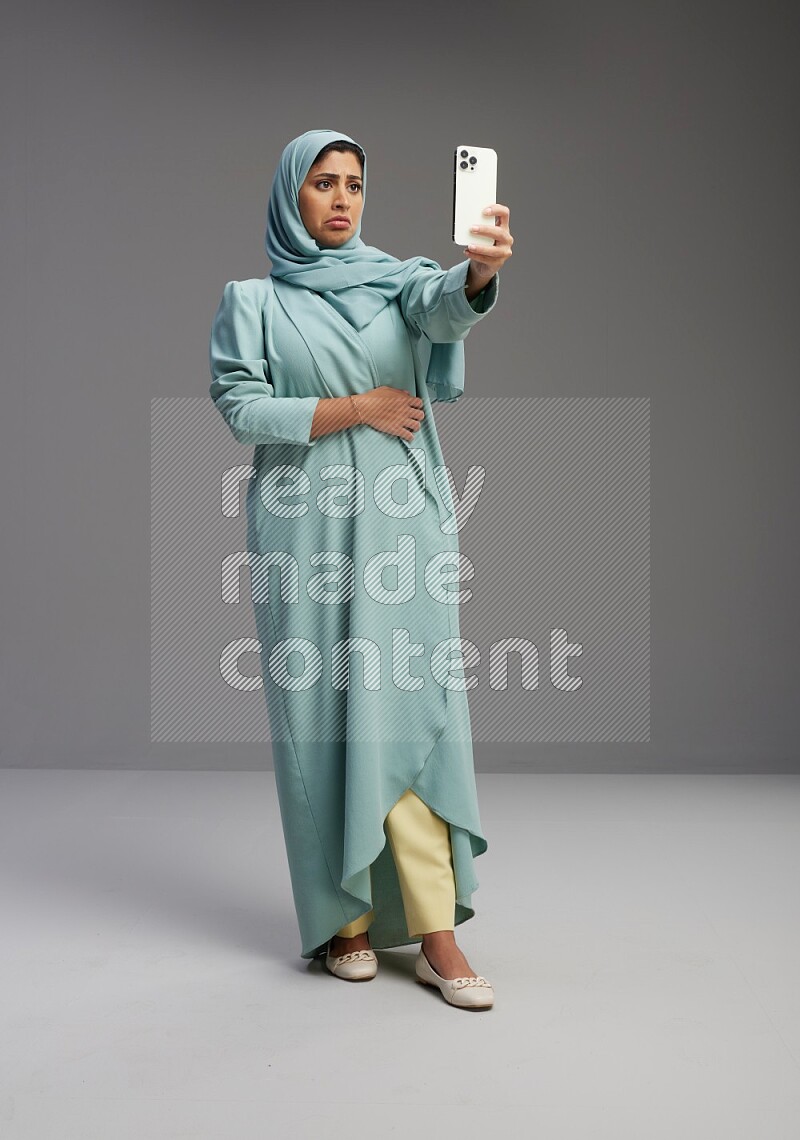 Saudi Woman wearing Abaya standing taking selfie on Gray background