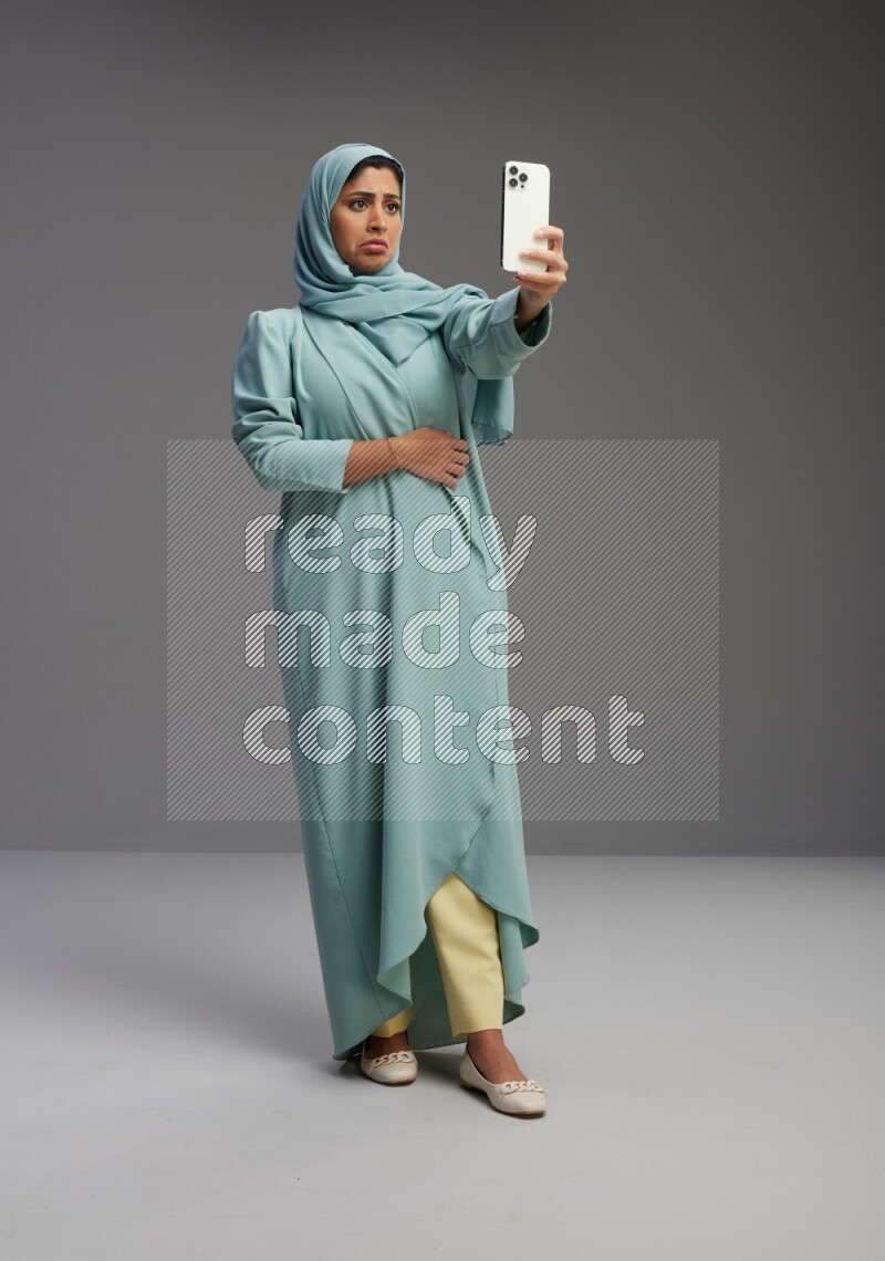 Saudi Woman wearing Abaya standing taking selfie on Gray background