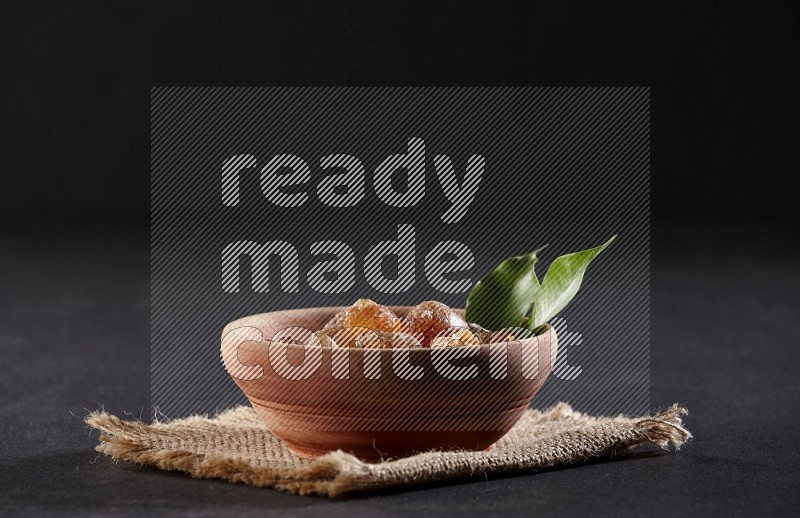 A wooden bowl full of gum arabic on a piece of burlap on black flooring in different angles