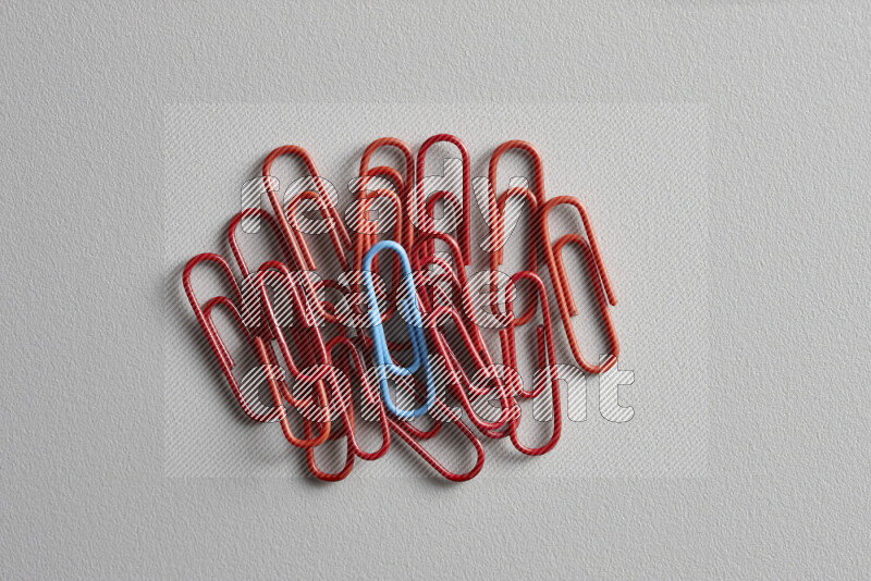 A blue paperclip surrounded by bunch of red paperclips on grey background