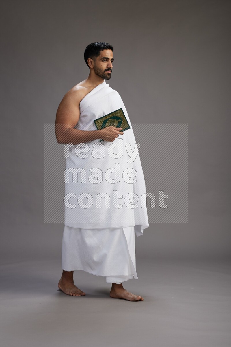 A man wearing Ehram Standing reading quran on gray background