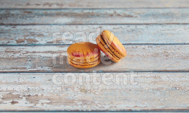 45º Shot of two orange Exotic macarons on light blue wooden background