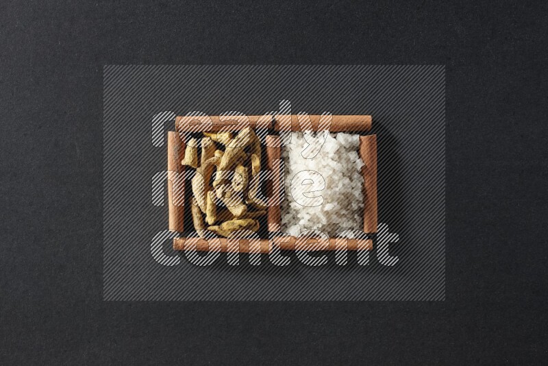 مربعان من أعواد القرفة ممتلئان بالملح الأبيض وأصابع الكركم علي خلفية سوداء
