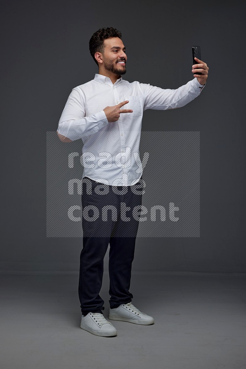 A man wearing smart casual and taking selfie with his phone eye level on a gray background