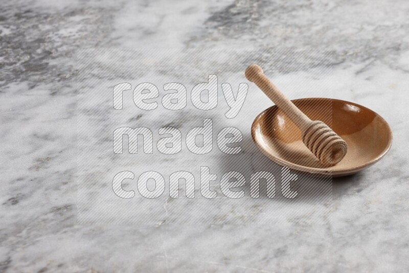 Multicolored pottery plate with wooden honey dipper in it on grey marble background