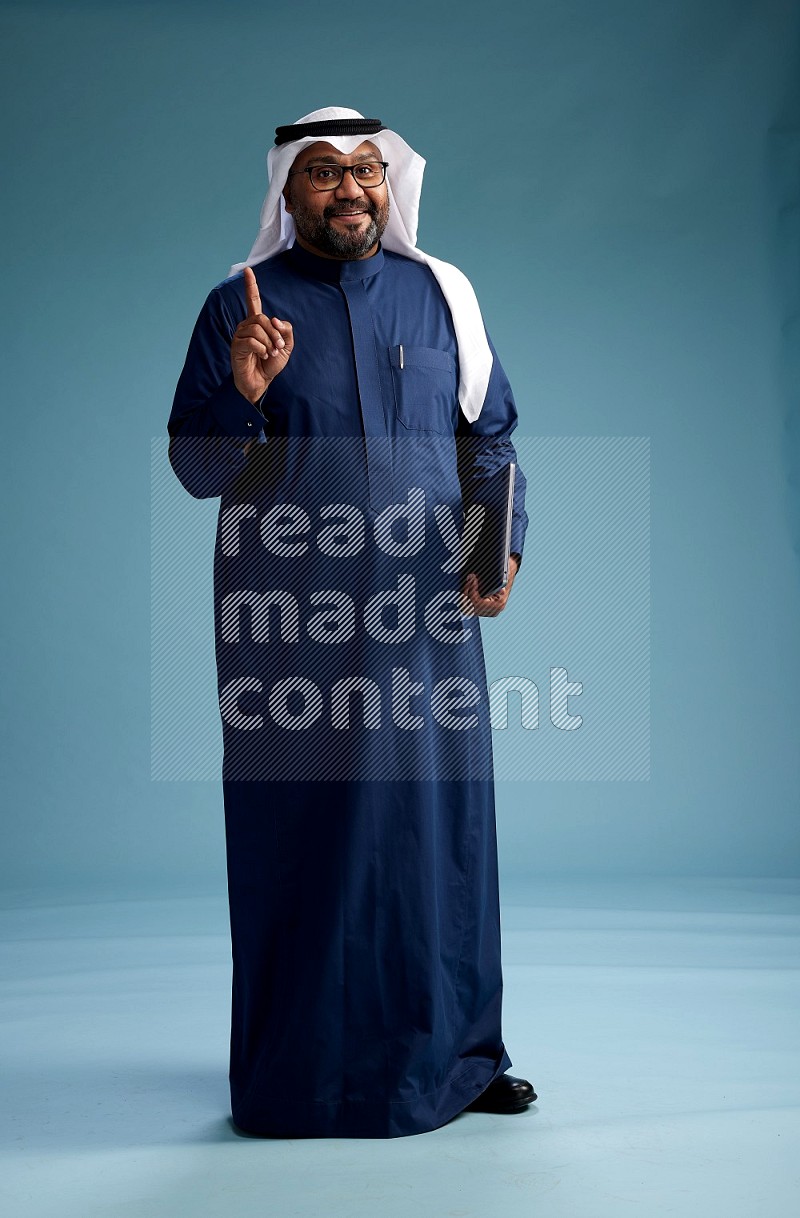 Saudi Man with shimag Standing working on laptop on blue background