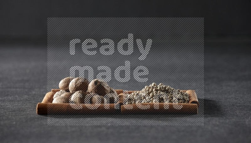 2 squares of cinnamon sticks full of nutmeg and white peppers on black flooring