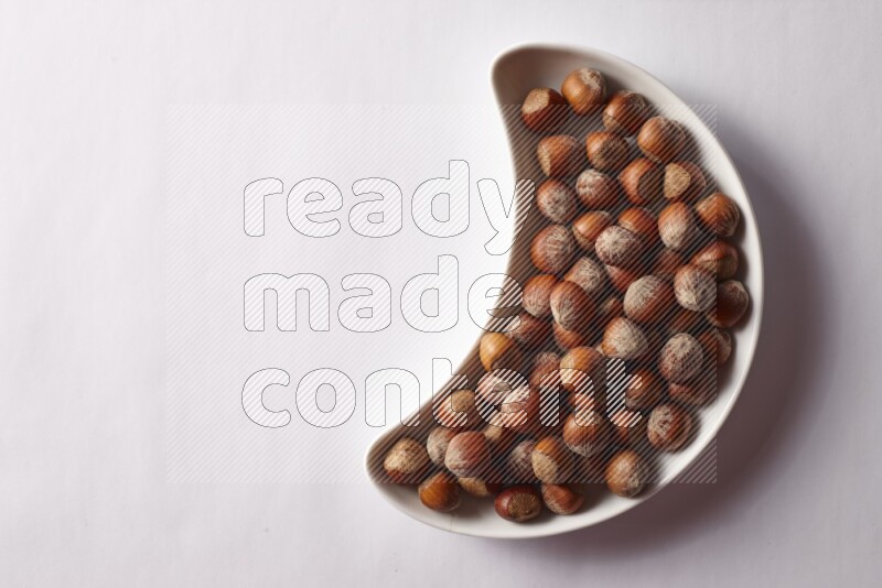 Hazelnuts in a crescent pottery plate on white background
