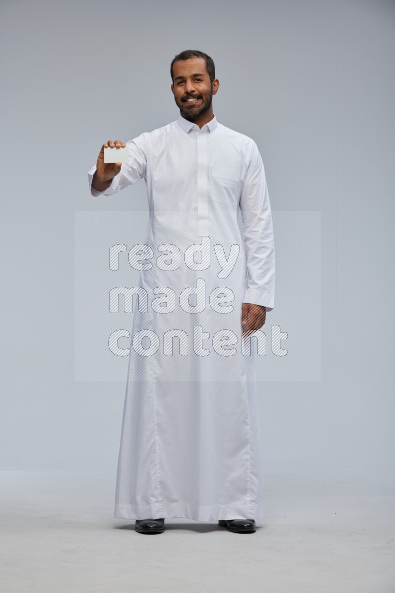 Saudi man wearing Thob standing holding ATM card on Gray background