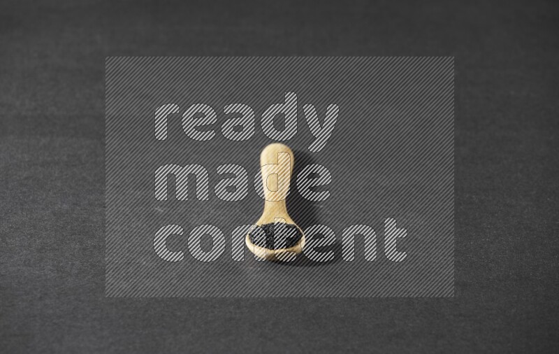 ملعقة خشبية ممتلئة بحبة البركة على أرضية سوداء