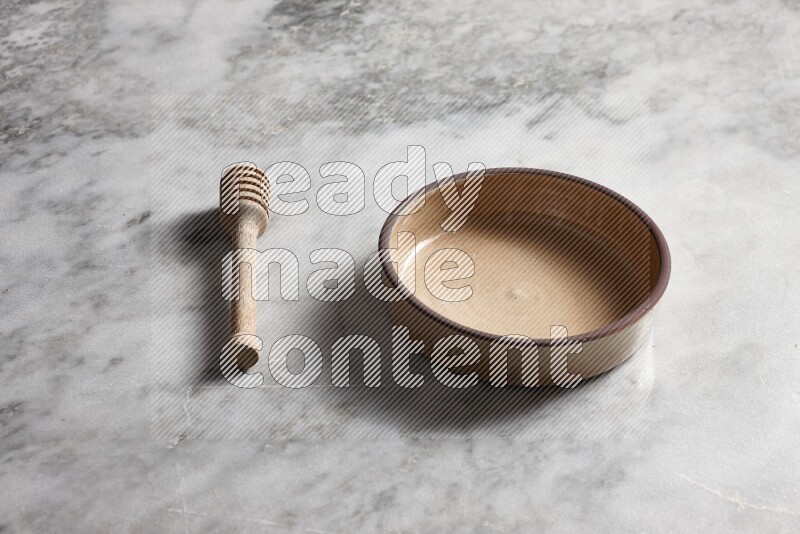 Beige pottery oven bowl with wooden honey dipper on the side on grey marble background