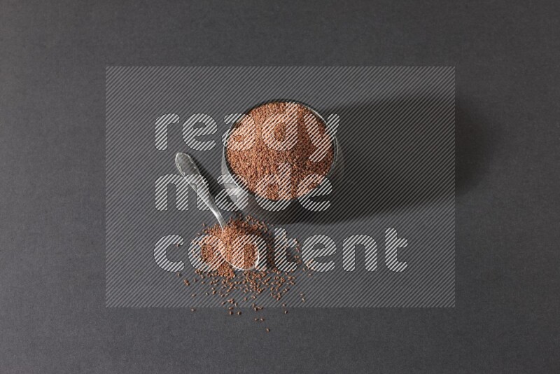 A black pottery bowl full of garden cress seeds and metal spoon full of the seeds on a black flooring