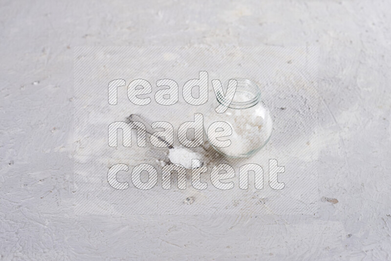 A glass jar full of coarse sea salt crystals on white background