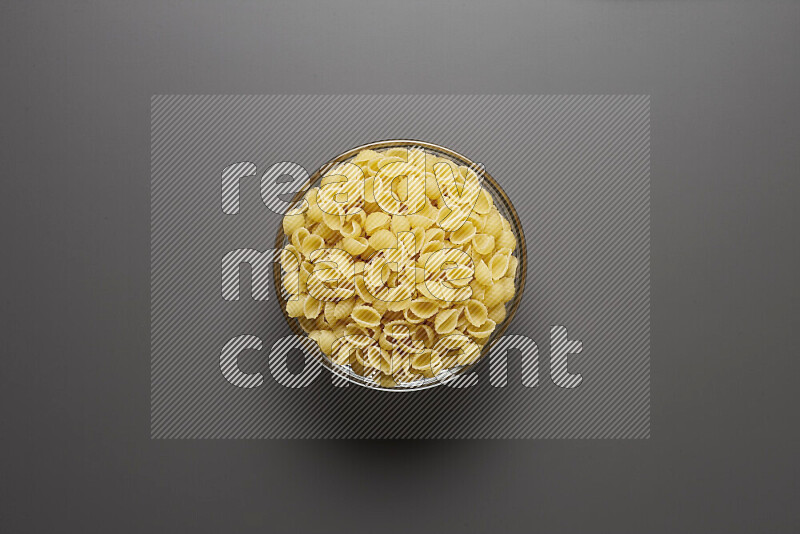 Shells pasta in a glass bowl on grey background