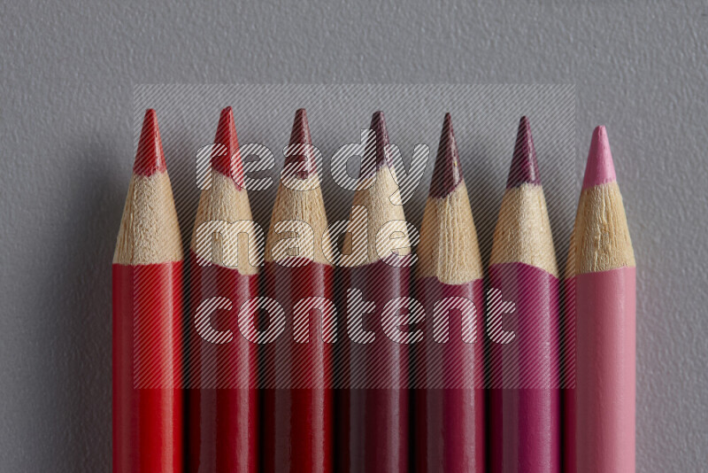 A collection of colored pencils arranged showcasing a gradient of pink and red hues on grey background