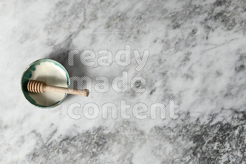 Multicolored Pottery Bowl with wooden honey handle in it, on grey marble flooring, Top View