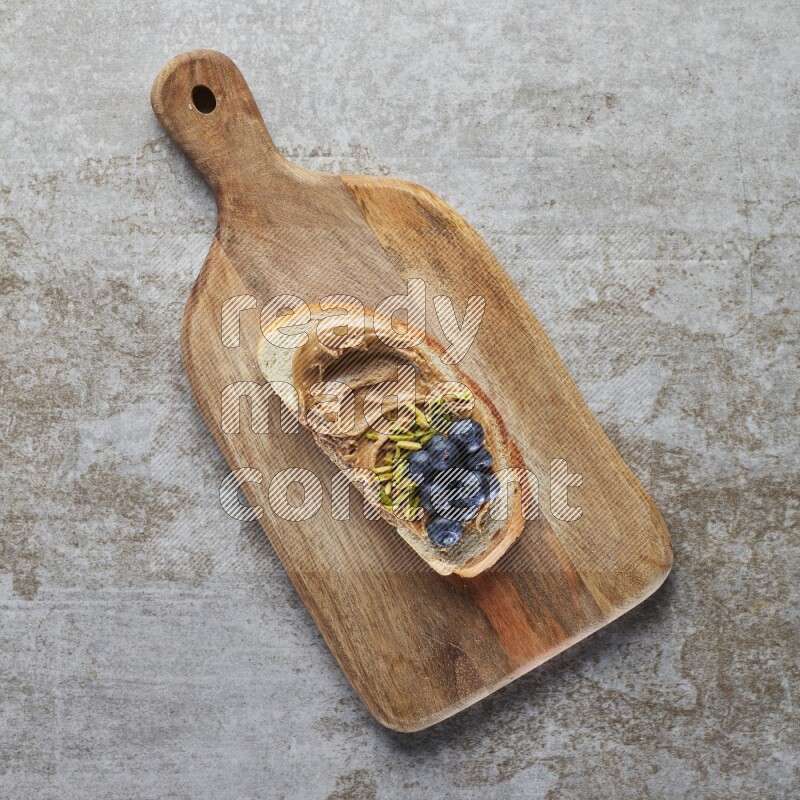open faced peanut butter sandwich with blueberries and pistachio on a grey textured background