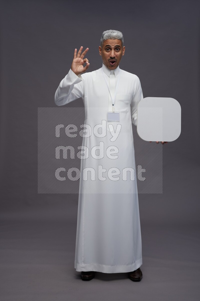 Saudi man wearing thob with neck strap employee badge standing holding social media sign on gray background