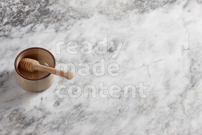 Beige Pottery oven bowl with wooden honey handle on the side with grey marble flooring, 65 degree angle