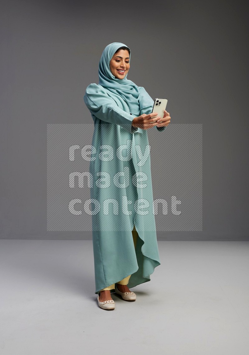 Saudi Woman wearing Abaya standing taking selfie on Gray background