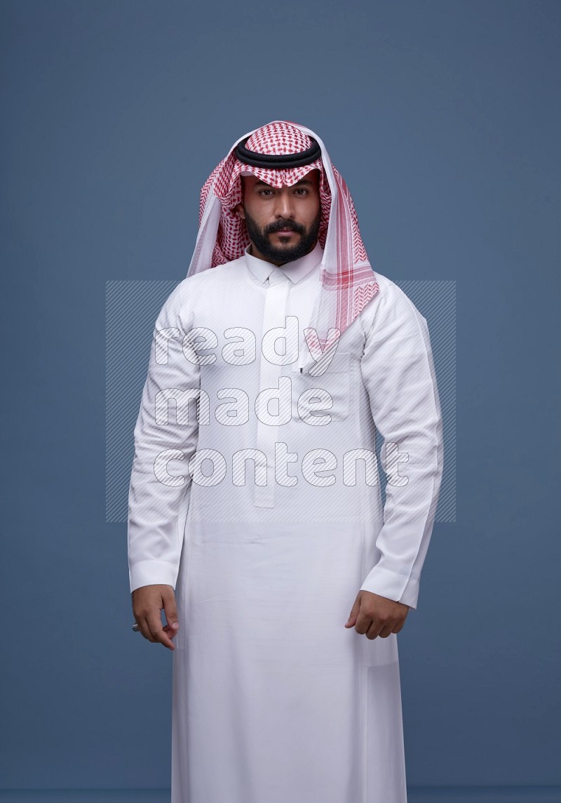 A Saudi man posing on blue background wearing Thob and Shomag