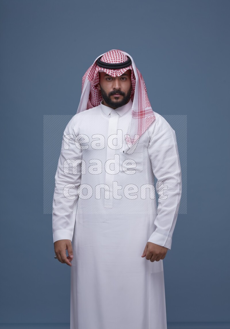 A Saudi man posing on blue background wearing Thob and Shomag