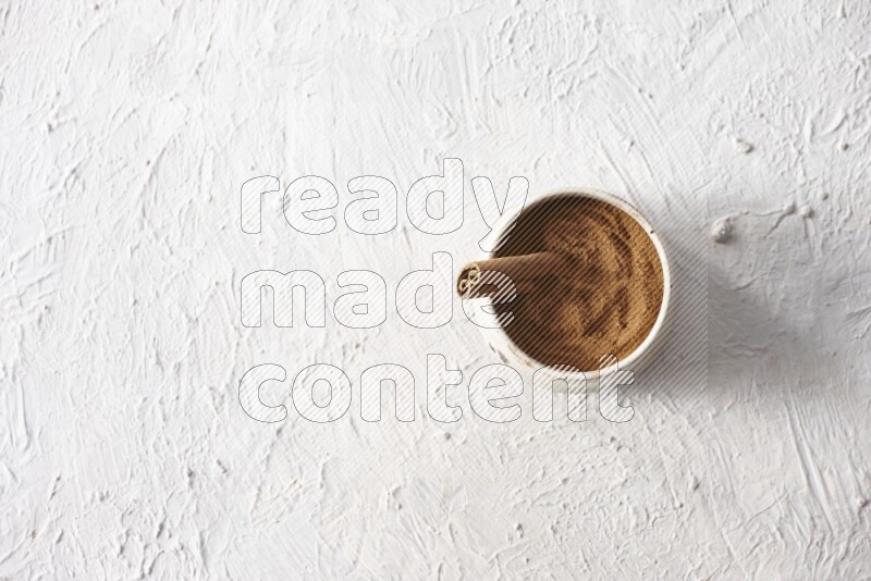 بودرة قرفة في وعاء بيج مع عود قرفة علي خلفية بيضاء