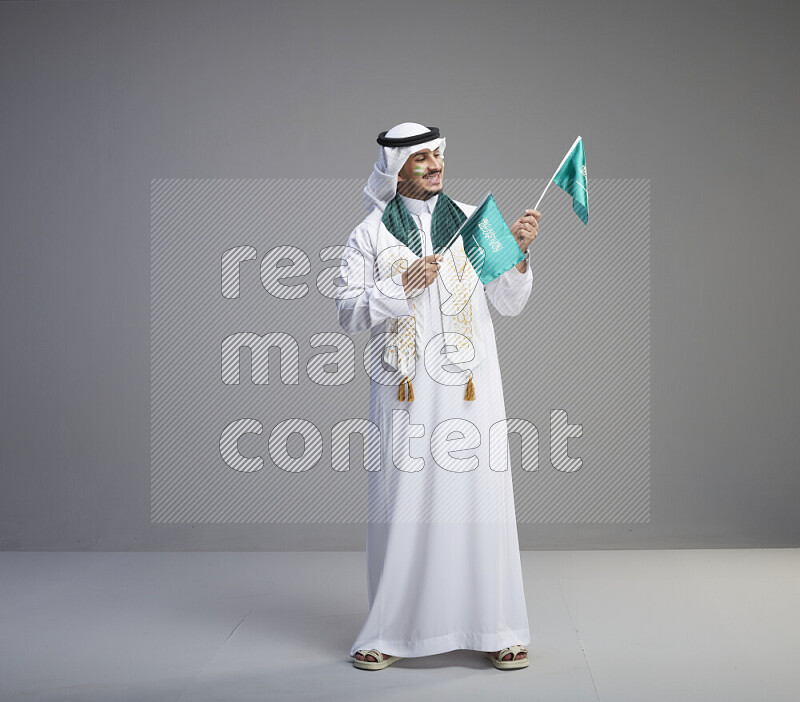 رجل سعودي يرتدي ثوب وشماغ ويحمل اعلام السعودية