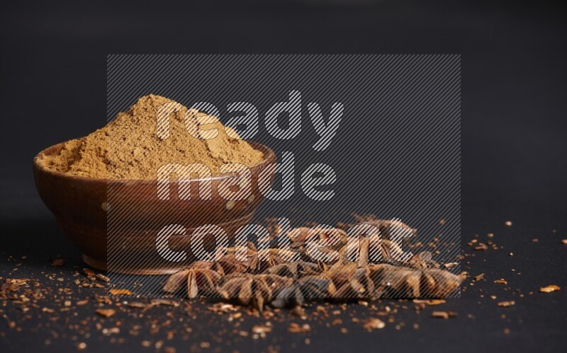 Star Anise powder in a wooden bowl with star anise beside it on a black background