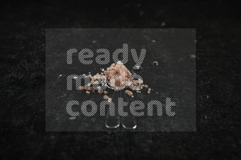 ملعقتان معدنيتان ممتلئتان بملح الهيمالايا الوردي على خلفية سوداء