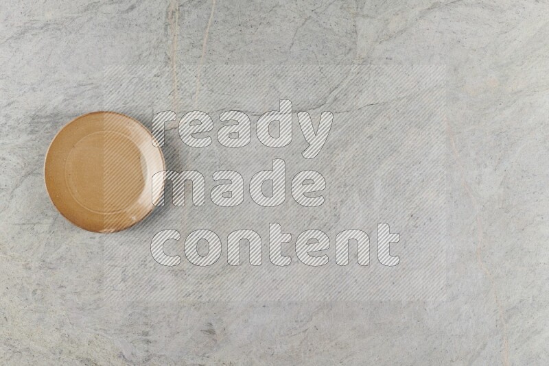 A circular beige pottery plate on grey marble background
