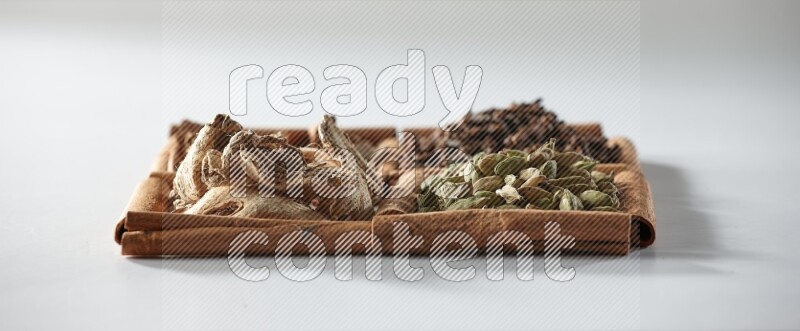 4 مربعات من أعواد القرفة ممتلئة بالهيل والقرفة والقرنفل والزنجبيل المجفف على أرضية بيضاء