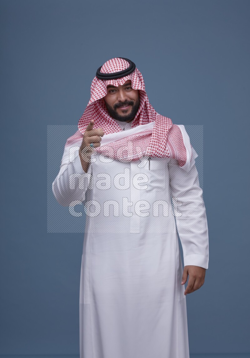 A Saudi man posing on blue background wearing Thob and Shomag