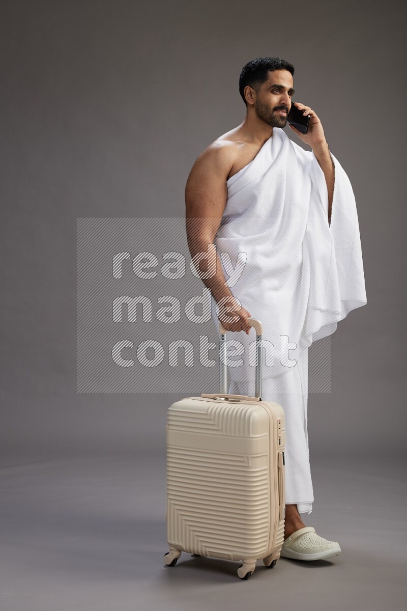 A man wearing Ehram Standing holding traveling bag on gray background