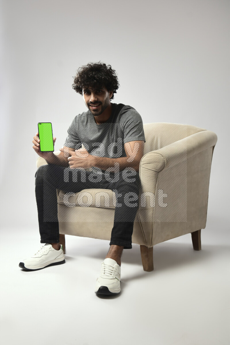 A man wearing casual sitting on a chair showing a phone screen on white background