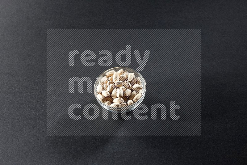 A glass bowl full of pistachios on a black background in different angles