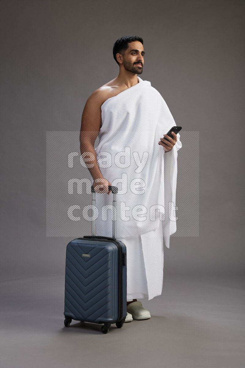 A man wearing Ehram Standing holding traveling bag on gray background