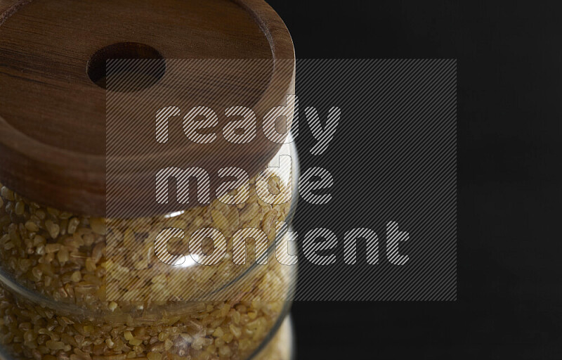 Coarse bulgur in a glass jar on black background