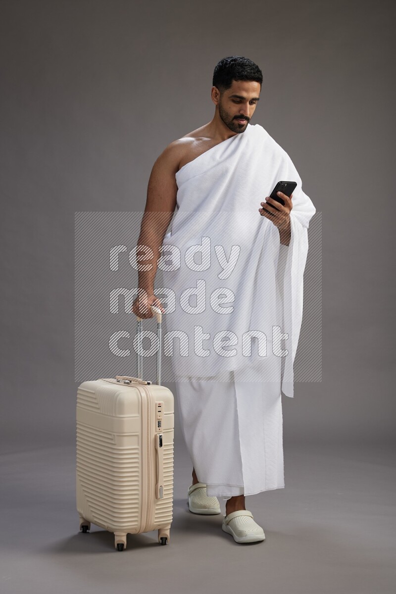 A man wearing Ehram Standing holding traveling bag on gray background