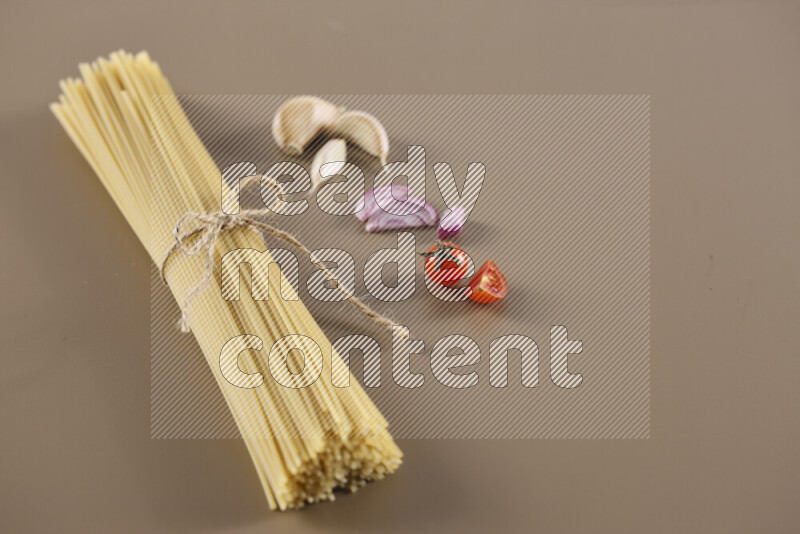 Raw pasta with different ingredients such as cherry tomatoes, garlic, onions, red chilis, black pepper, white pepper, bay laurel leaves, rosemary and cardamom on beige background