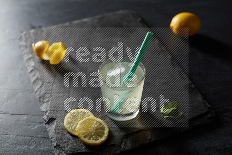 A glass of lemon juice with a straw on black background