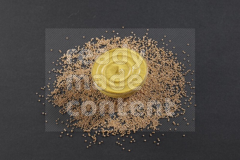 وعاء زجاجي مملوء بمعجون الخردل مع بذور الخردل تحته على أرضية سوداء