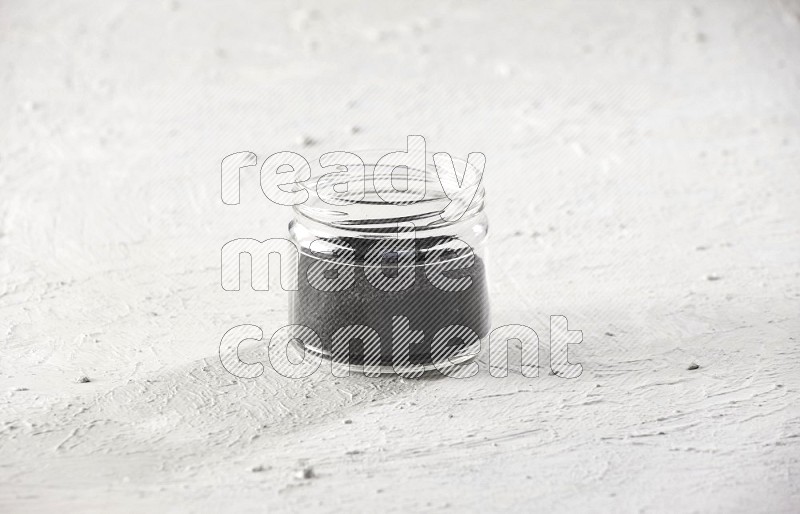 A glass jar full of black seeds on a textured white flooring in different angles