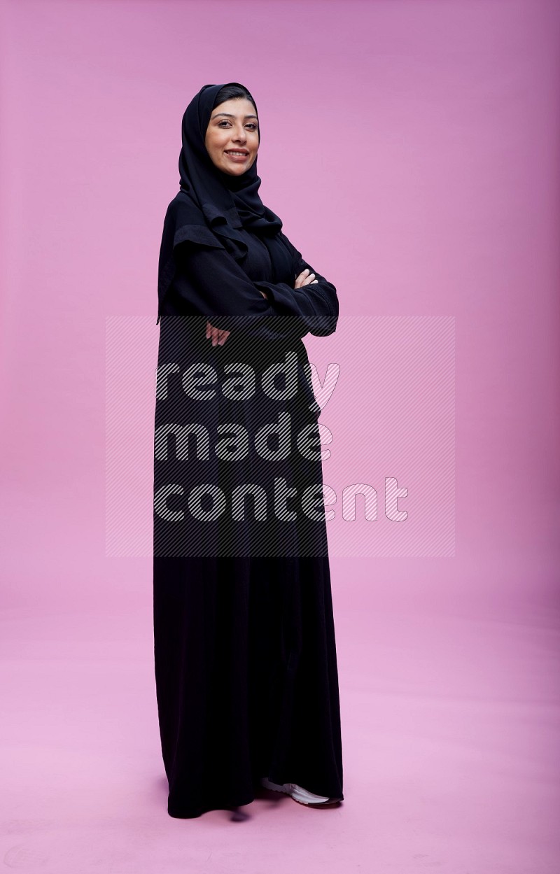 Saudi woman wearing Abaya standing with crossed arms on pink background