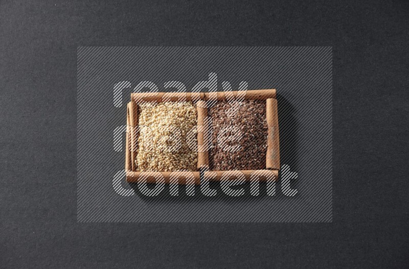 مربعان من أعواد القرفة ممتلئان ببذور الكتان وبذور السمسم علي خلفية سوداء