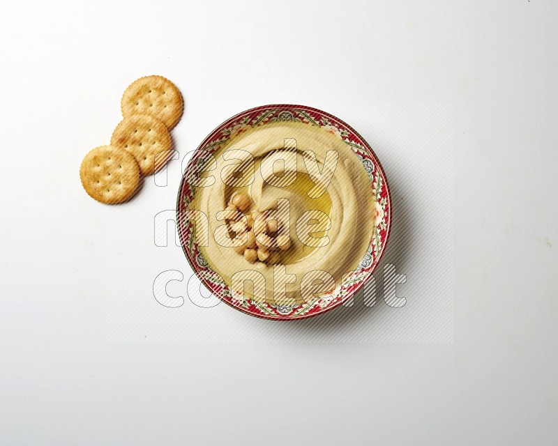 Hummus in a red plate with patterns garnished with roasted chickpeas  on a white background