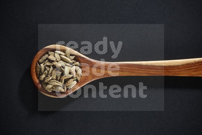 A wooden ladle full of cardamom on black flooring
