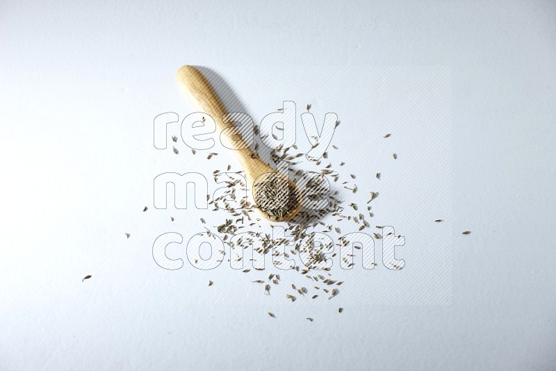 A wooden spoon full of cumin seeds on a white flooring