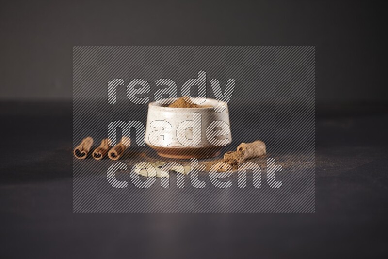 Cinnamon powder in a white pottery bowl and cinnamon sticks and laurel leaves on black background