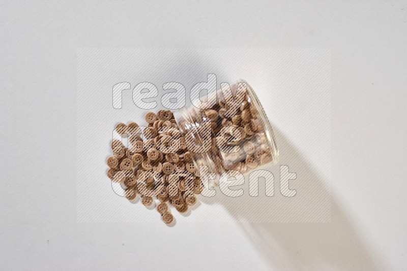 A glass jar full of colored buttons on grey background